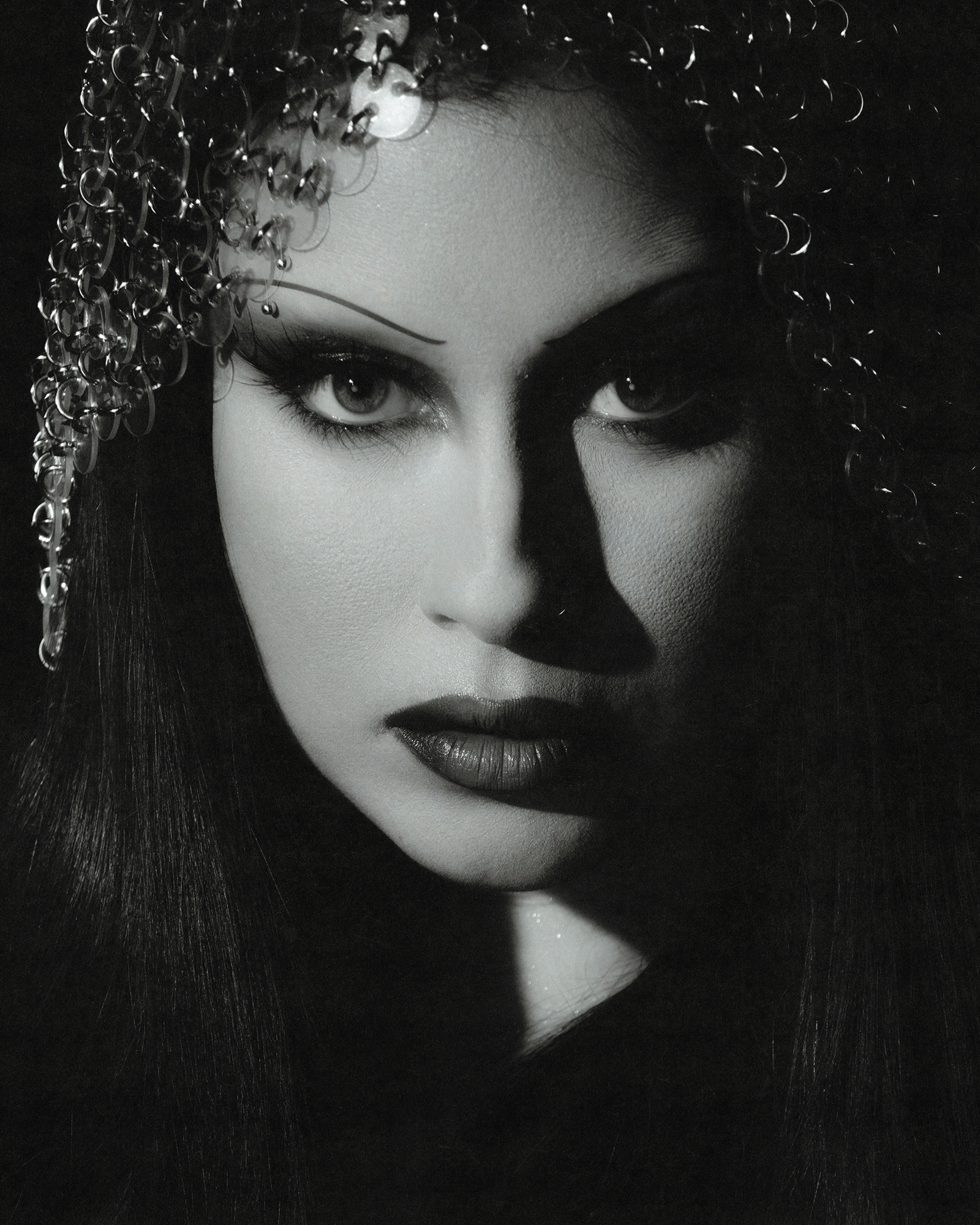 Close up black and white portriat of Lauren Juaregui with a chainmail headdress, dramatic eye makeup, thin brows and dark lips